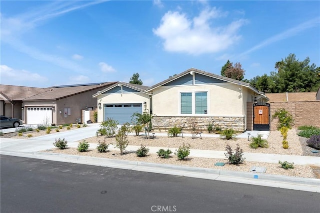 view of front of property with stucco siding, an attached garage, stone siding, driveway, and a gate