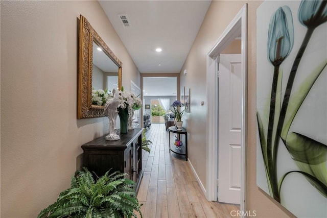 corridor featuring light wood finished floors, baseboards, and visible vents