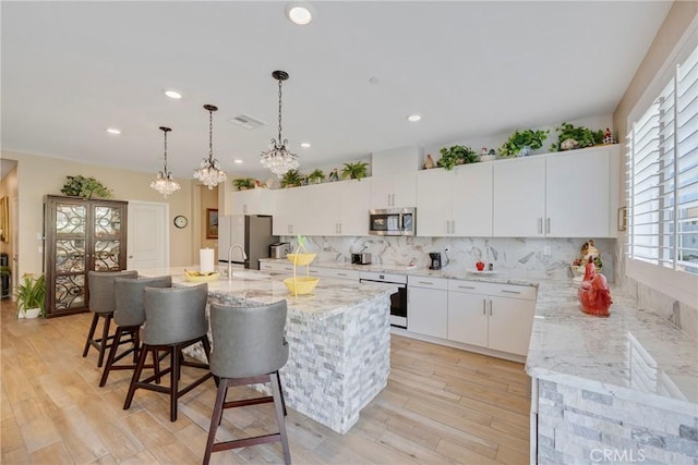 kitchen with a sink, backsplash, a kitchen bar, appliances with stainless steel finishes, and a center island with sink