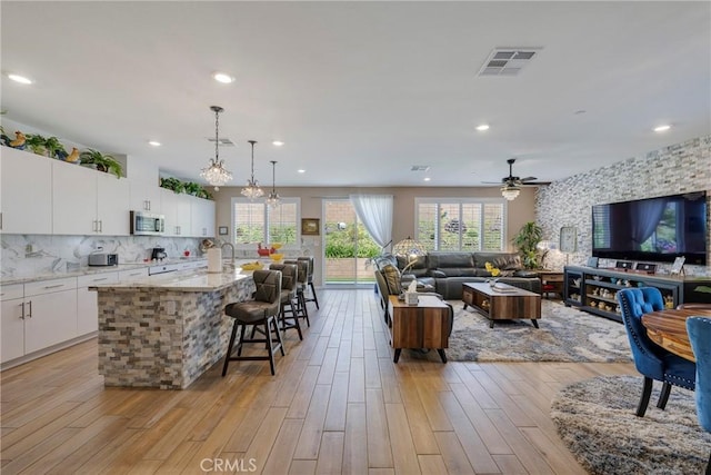 kitchen with white cabinetry, tasteful backsplash, a kitchen bar, stainless steel microwave, and visible vents
