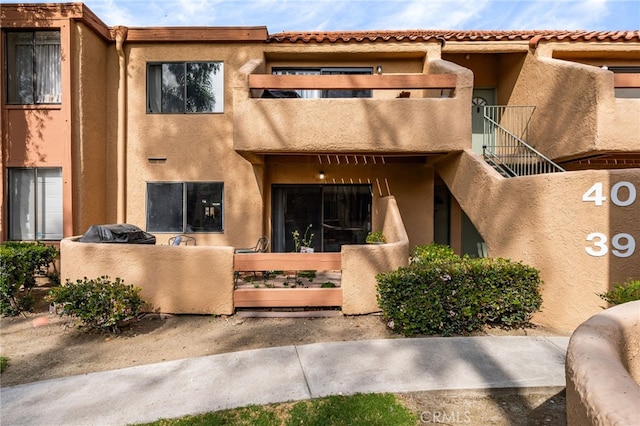 view of front of property featuring stairs, stucco siding, a tiled roof, and fence