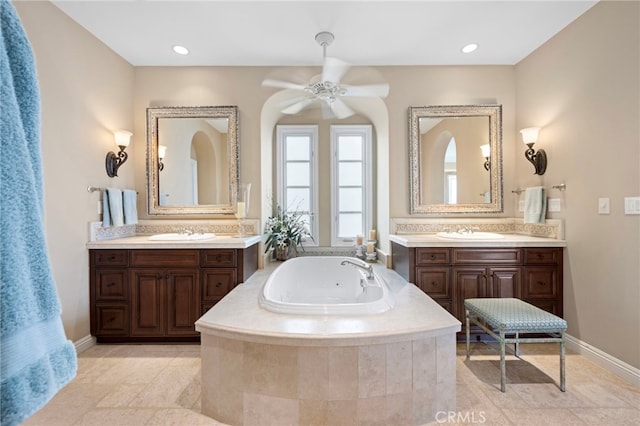 bathroom featuring a jetted tub, ceiling fan, a sink, and two vanities