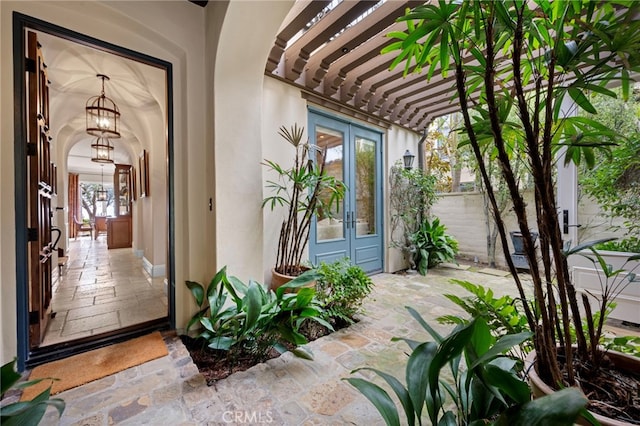 view of exterior entry featuring french doors, a pergola, and stucco siding