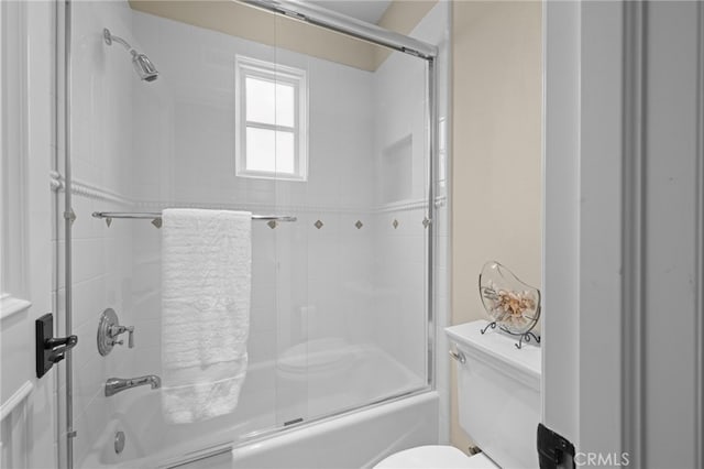 bathroom featuring toilet and shower / bath combination with glass door