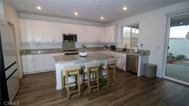 kitchen with appliances with stainless steel finishes, white cabinets, a kitchen island, and dark wood finished floors