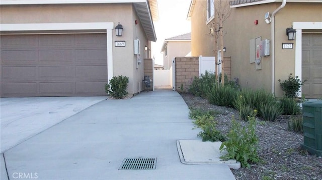 exterior space featuring concrete driveway, a garage, fence, and stucco siding