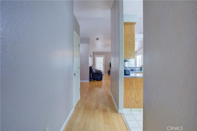 hall with light wood finished floors, baseboards, and a textured wall