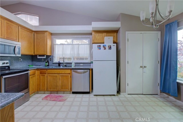 kitchen featuring vaulted ceiling, a sink, light floors, appliances with stainless steel finishes, and an inviting chandelier