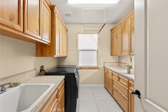 laundry room featuring cabinet space, washing machine and clothes dryer, a sink, baseboards, and light tile patterned flooring