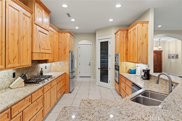 kitchen with appliances with stainless steel finishes, a sink, tasteful backsplash, and arched walkways