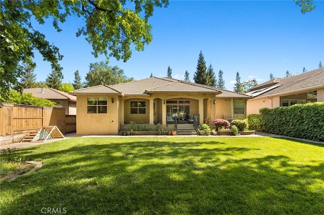 rear view of property with fence, a lawn, stucco siding, and a tile roof
