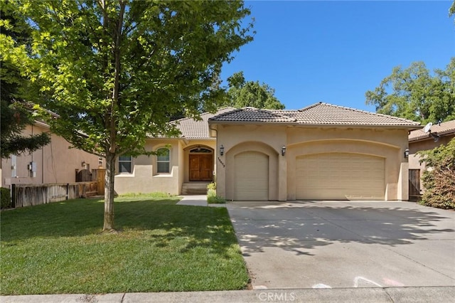mediterranean / spanish-style home featuring driveway, a tiled roof, a front yard, an attached garage, and stucco siding