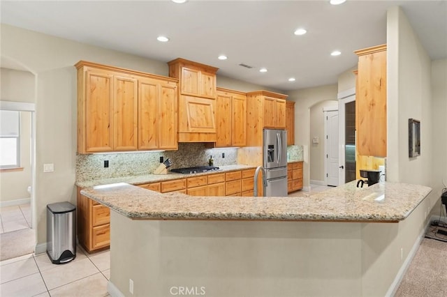 kitchen featuring arched walkways, decorative backsplash, stainless steel fridge with ice dispenser, gas stovetop, and baseboards