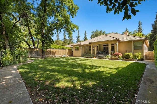 rear view of property with a fenced backyard, a lawn, a tiled roof, a chimney, and stucco siding