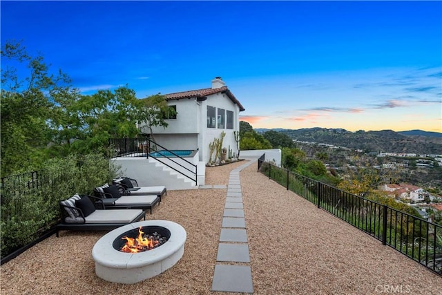 back of house with stucco siding, fence, a mountain view, a fire pit, and a chimney