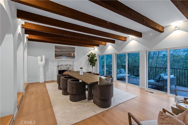dining space with visible vents, a premium fireplace, light wood-type flooring, and beam ceiling
