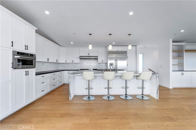 33781 Copper Lantern St, Dana Point, CA 92629 - kitchen with under cabinet range hood, white cabinetry, a kitchen breakfast bar, backsplash, and appliances with stainless steel finishes