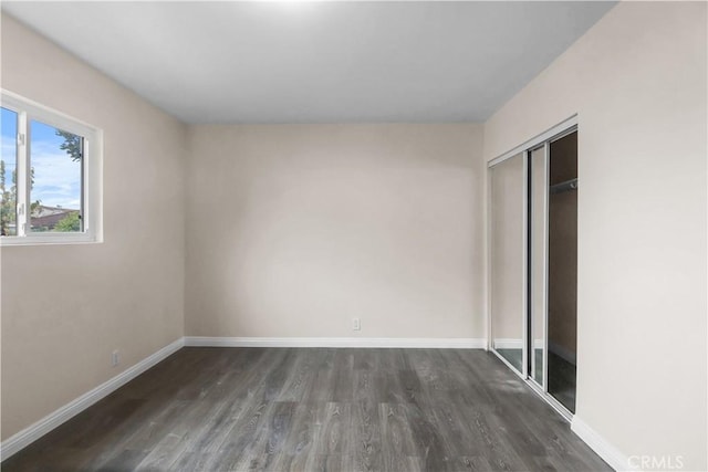 unfurnished bedroom with dark wood finished floors, baseboards, and a closet