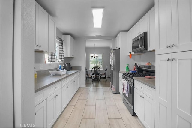 kitchen featuring a sink, an inviting chandelier, stainless steel appliances, white cabinetry, and baseboards