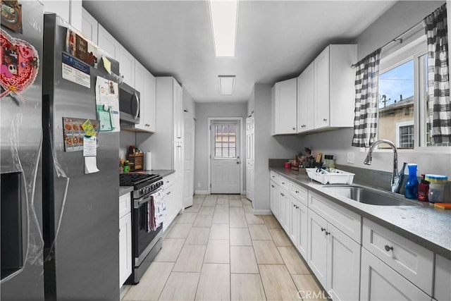kitchen featuring appliances with stainless steel finishes, white cabinetry, baseboards, and a sink