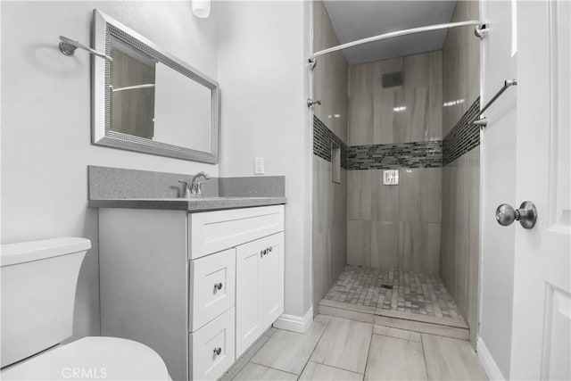 bathroom featuring baseboards, a tile shower, toilet, and vanity