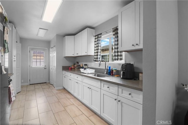 kitchen featuring a sink, baseboards, white cabinetry, and plenty of natural light