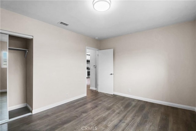 unfurnished bedroom with a closet, visible vents, wood finished floors, and baseboards