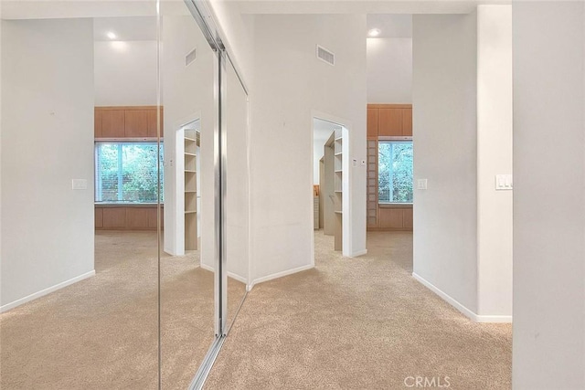 hall with a high ceiling, light carpet, visible vents, and baseboards