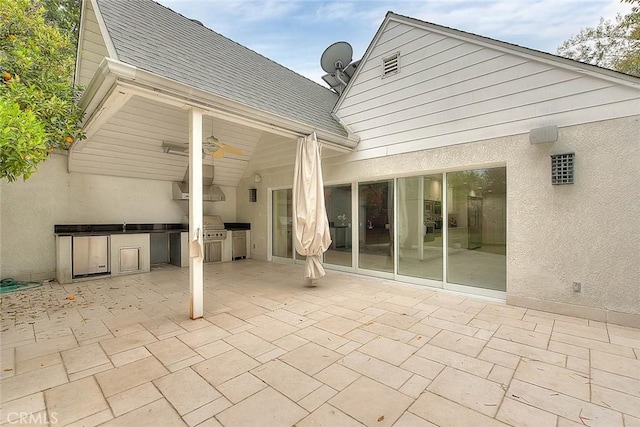 rear view of house featuring stucco siding, roof with shingles, an outdoor kitchen, and ceiling fan