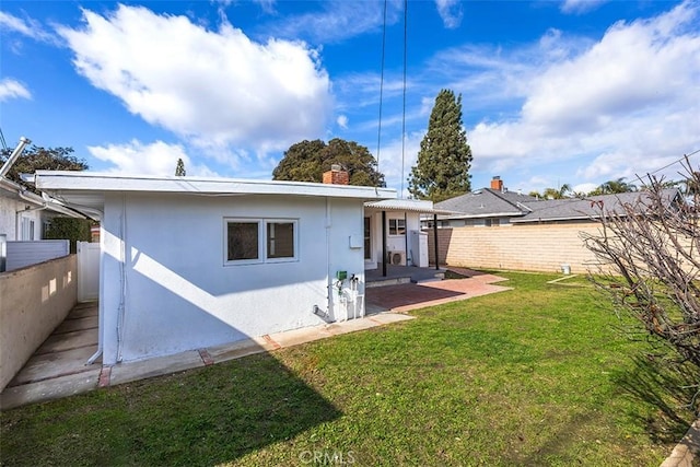 rear view of property with fence, a patio, stucco siding, and a lawn