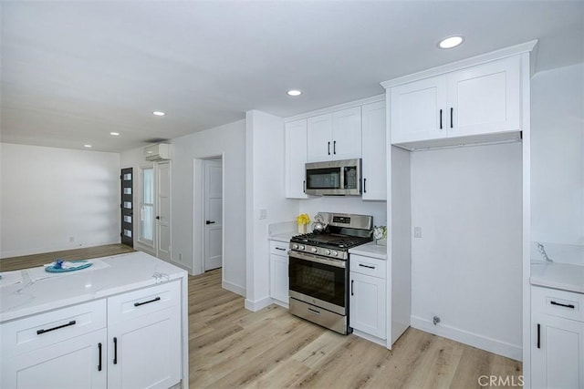 kitchen with light wood-style floors, a wall mounted air conditioner, appliances with stainless steel finishes, and white cabinets