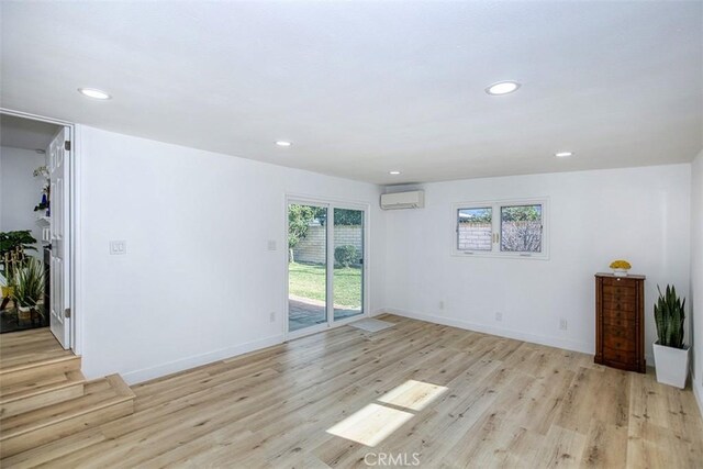 unfurnished living room with an AC wall unit, a wealth of natural light, and light wood-style floors