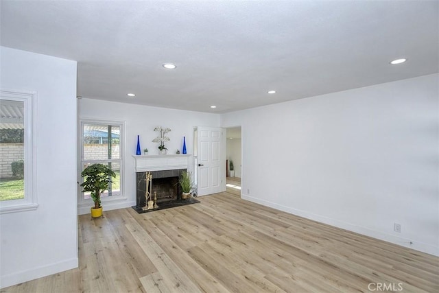 unfurnished living room with baseboards, a fireplace, recessed lighting, and light wood-style flooring