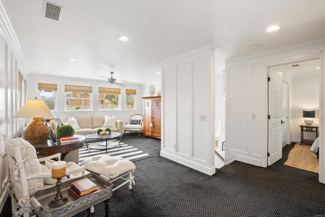 living room featuring visible vents, dark colored carpet, ornamental molding, and a ceiling fan