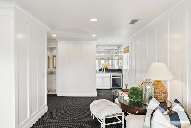 living area with a decorative wall, visible vents, dark colored carpet, and beverage cooler