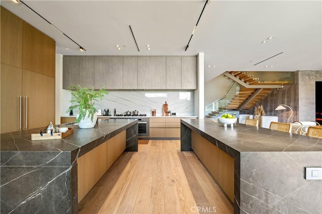 kitchen with dark countertops, modern cabinets, decorative backsplash, and light wood-type flooring