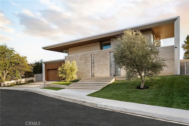 modern home with stone siding, an attached garage, concrete driveway, a front lawn, and stucco siding