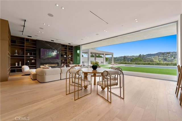 dining room with a glass covered fireplace, recessed lighting, floor to ceiling windows, built in features, and wood finished floors