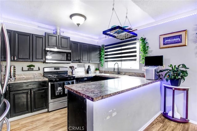 7801 Pinyon Ave, Fontana, CA 92336 - kitchen featuring light wood-style flooring, a peninsula, appliances with stainless steel finishes, a sink, and dark cabinets