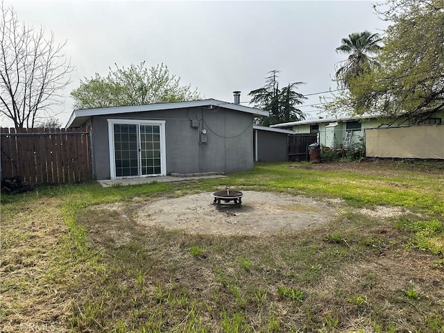 back of property with a fire pit, stucco siding, fence, and a yard