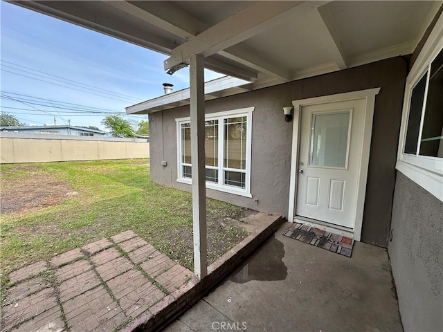 doorway to property featuring stucco siding, fence, and a lawn