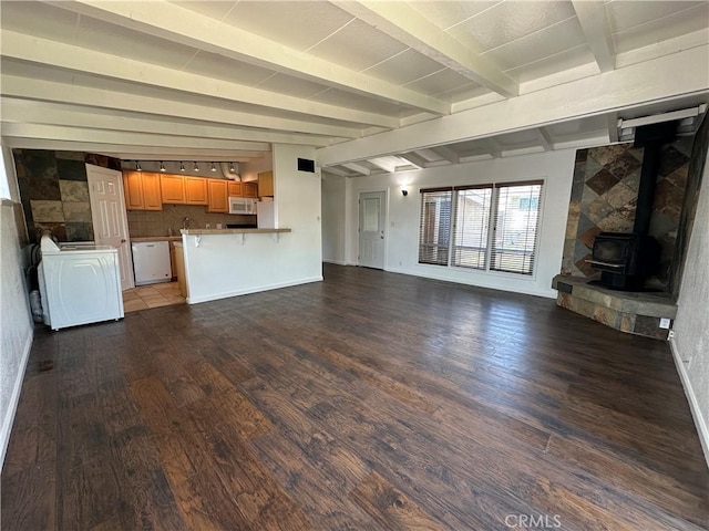 unfurnished living room featuring a wood stove, baseboards, washer / dryer, vaulted ceiling with beams, and wood finished floors