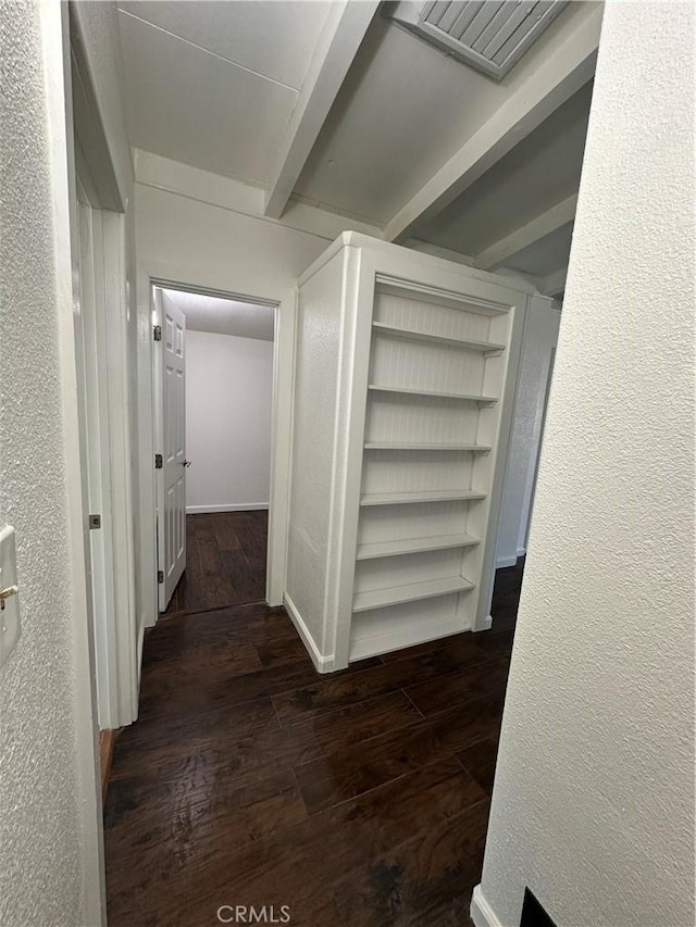 corridor featuring a textured wall, baseboards, wood finished floors, and beam ceiling