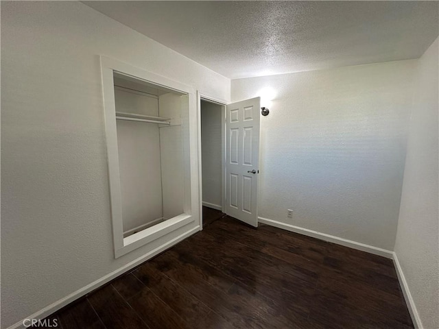 unfurnished bedroom with a closet, a textured ceiling, baseboards, and wood finished floors