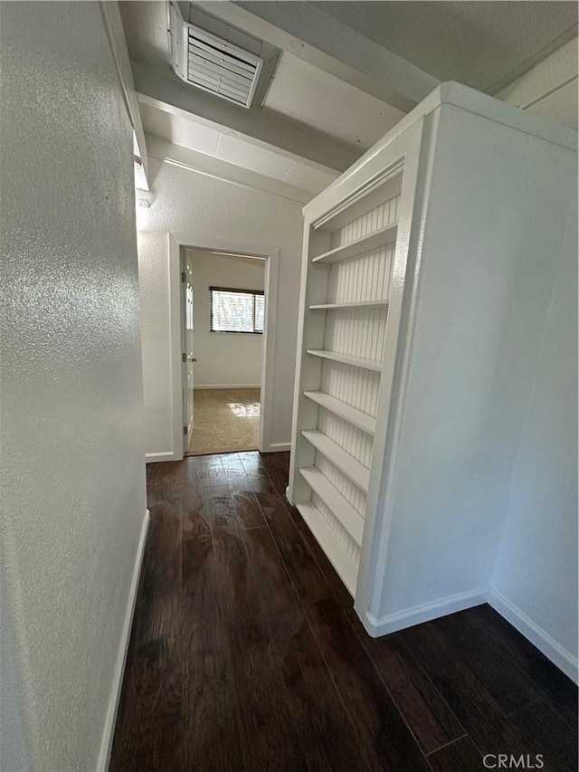 hall featuring vaulted ceiling with beams, wood finished floors, baseboards, visible vents, and a textured wall