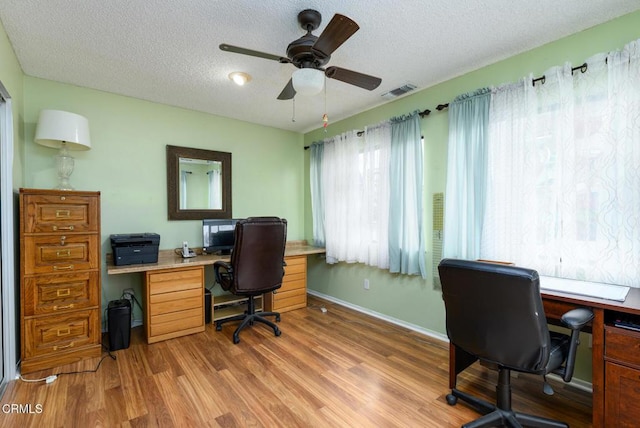 office space with light wood finished floors, visible vents, a textured ceiling, and a ceiling fan