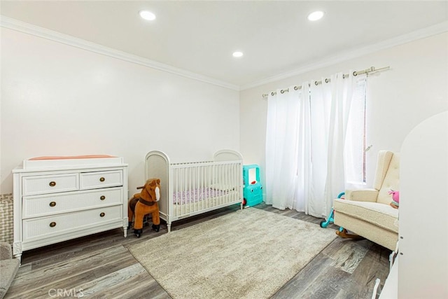 bedroom featuring recessed lighting, wood finished floors, ornamental molding, and a nursery area