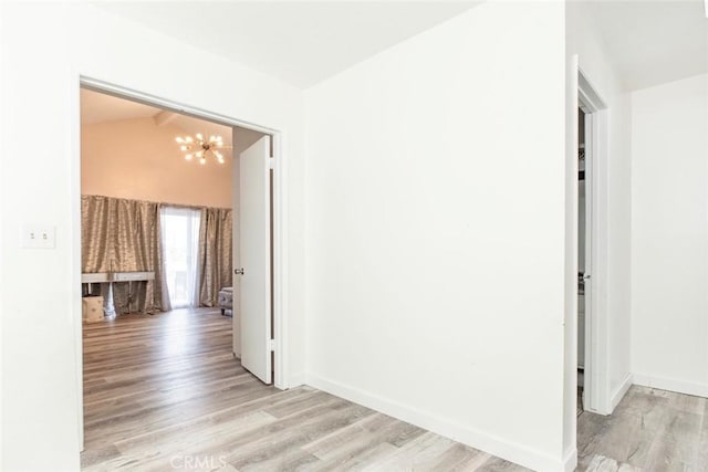 hallway featuring baseboards, light wood-style flooring, and a notable chandelier