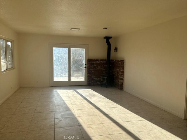 unfurnished living room with a textured ceiling, a wood stove, baseboards, tile patterned flooring, and visible vents