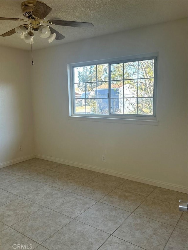 empty room with baseboards, a ceiling fan, a textured ceiling, and light tile patterned floors